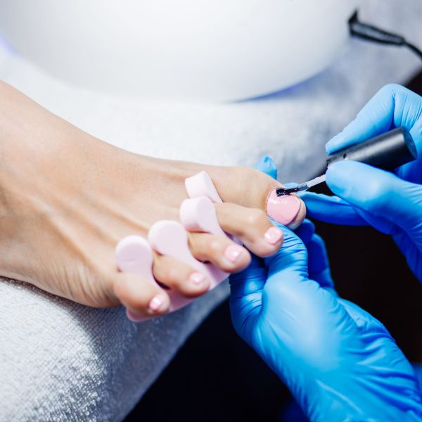 process-professional-pedicure-with-master-blue-gloves-applying-light-pink-gel-polish